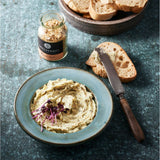 Eine Schale mit Kräuterbutter und daneben ein Brot mit Messer.