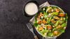 Knackiger Caesar Salad in einem tiefen Teller, daneben Serviette und Gabel.