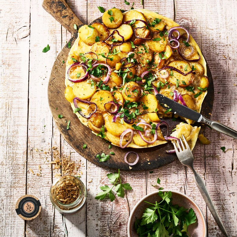 Bratkartoffelgewürz Korkenglas neben Bauernfrüstück, angerichtet auf einer Holzplatte.