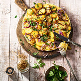 Bratkartoffelgewürz Korkenglas neben Bauernfrüstück, angerichtet auf einer Holzplatte.