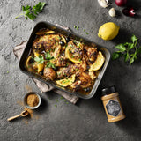 Africa Desert Dust Gewürzstreuer neben Hähnchen mit Zitronen und Oliven in Auflaufform, gewürzt und serviert auf dunklem Tisch.