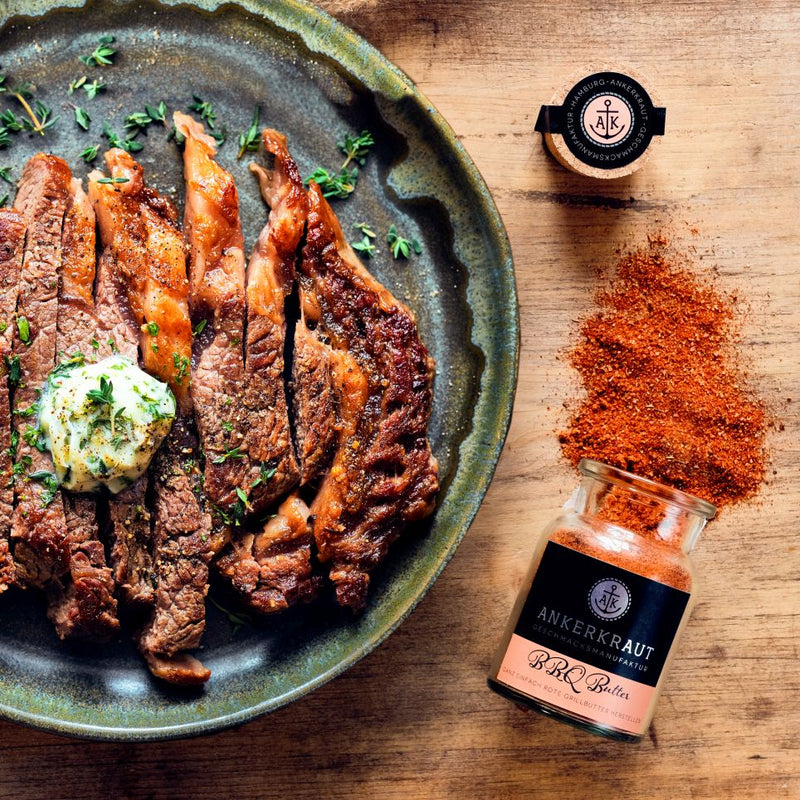 Gegrilltes Steak mit Kräuterbutter auf Teller, daneben BBQ-Gewürzglas und Gewürzstreuung auf Holzoberfläche.
