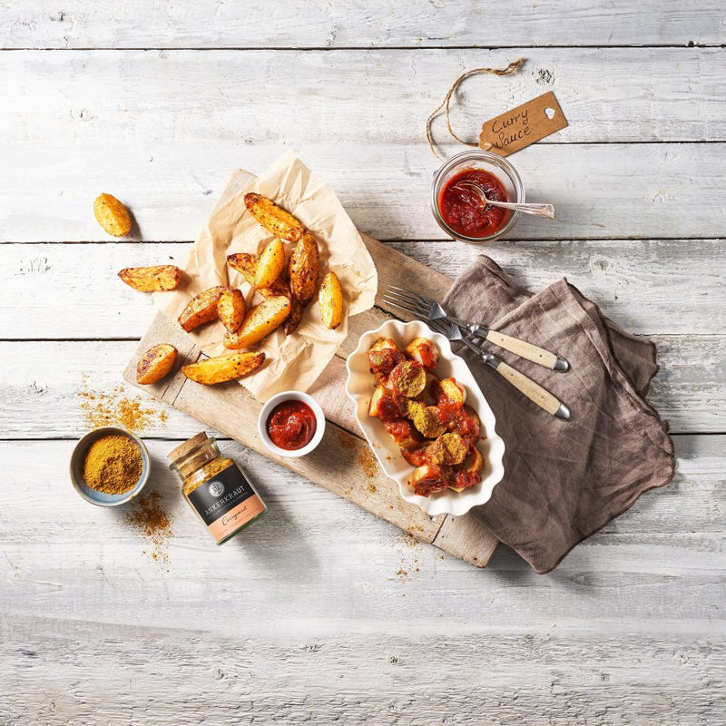 Currywurst im Schälchen mit Currywurst Gewürz als Topping und Kartoffelspalten als Beilage.