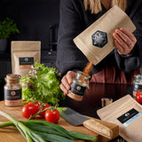 Magic Dust Rub wird von einer Frau von einem Nachfüllbeutel ins Korkenglas umgefüllt.