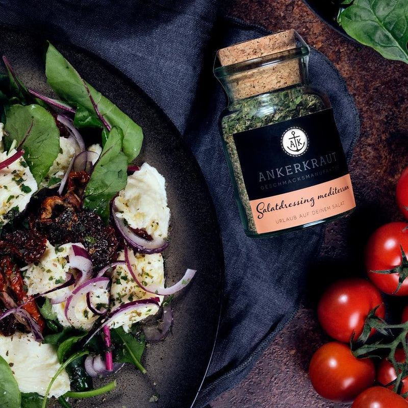 Korkenglas mit mediterranem Salatdressing neben einem frisch angerichteten Salat auf einem dunklen Teller.