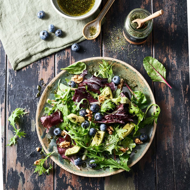 Salatgewürz im Korkenglas neben einem Sommersalat auf einem Tonteller.