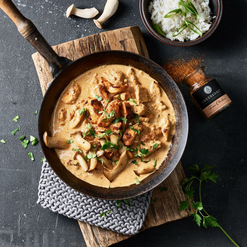 Hähnchenpfanne mit Pilzen in einer gußeisernen Pfanne auf einem Holzbrett.